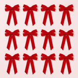 Twelve red velvet Christmas bows with long angled tails are arranged in three rows of four on a pale pink background.