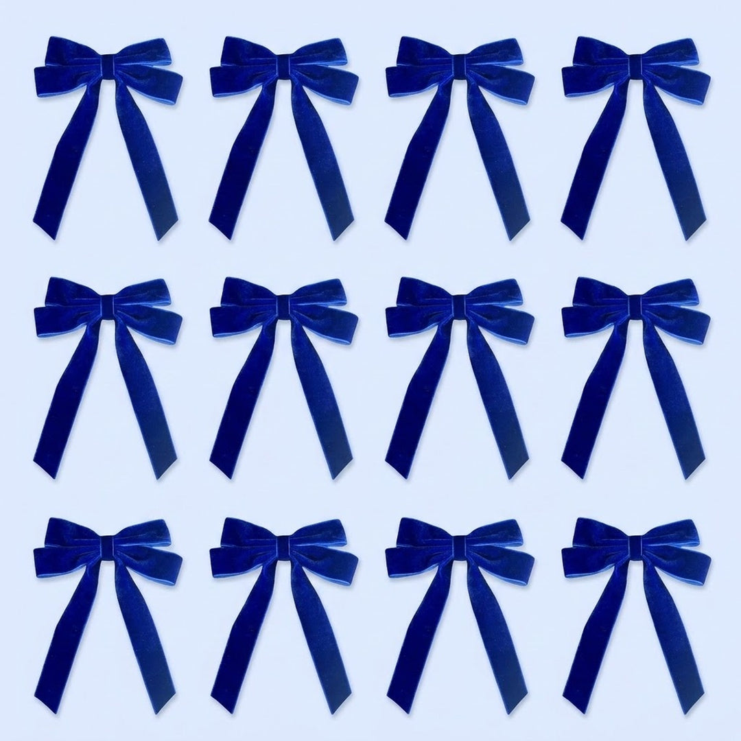 Twelve royal blue velvet Christmas bows with long tails are arranged in three rows of four on a pale blue background.