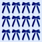 Twelve royal blue velvet Christmas bows with long tails are arranged in three rows of four on a pale blue background.