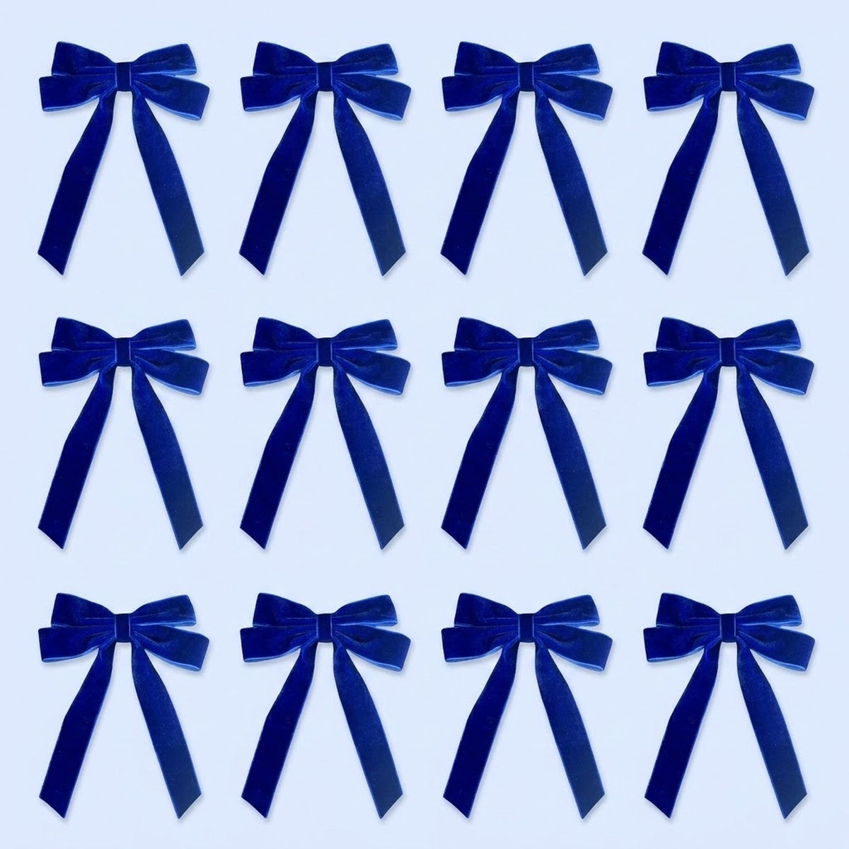 Twelve royal blue velvet Christmas bows with long tails are arranged in three rows of four on a pale blue background.