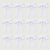 Twelve white velvet Christmas bows with long angled tails are arranged in three rows of four on a light gray background.