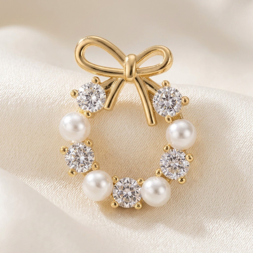 A gold-tone bow stud earring with white pearl-like beads and clear faceted stones rests on folded cream satin.