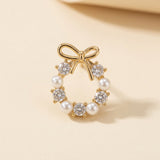 A gold-tone bow stud earring with white pearl-like beads and clear faceted stones stands on beige beneath a blurred raised edge.