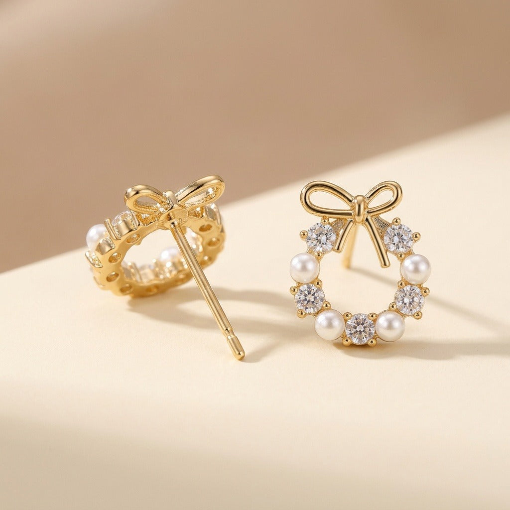 Two gold-tone bow stud earrings with pearl-like beads and clear stones show front and rear views on beige, with one post exposed.