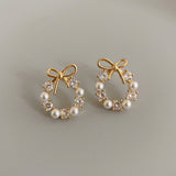 Stud earrings with gold-tone bows, white pearl-like beads and clear faceted stones rest side by side on a light gray surface.