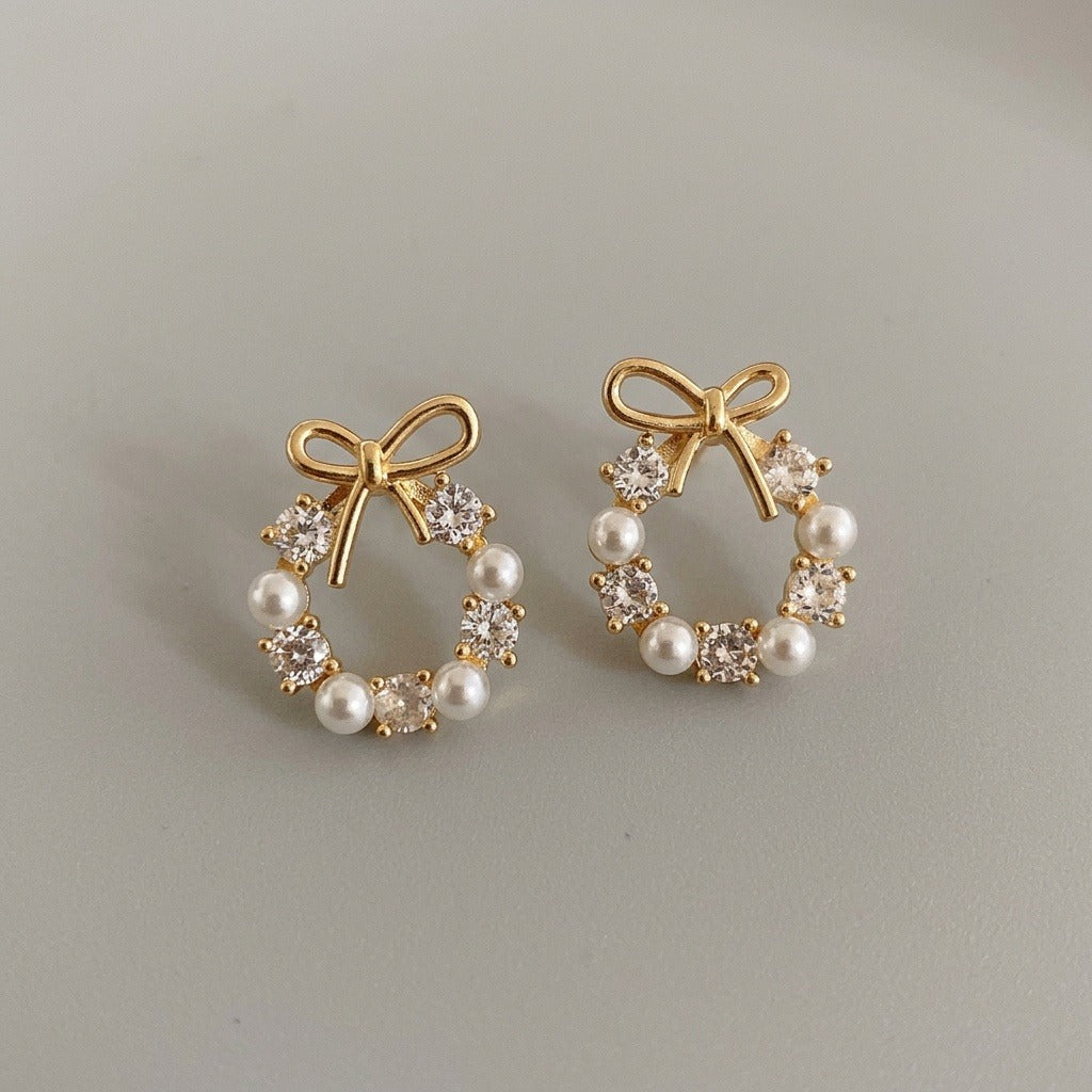 Stud earrings with gold-tone bows, white pearl-like beads and clear faceted stones rest side by side on a light gray surface.