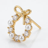 Gold-tone wreath-shaped stud earring with a bow, white pearl-like beads, and clear faceted stones on a white background.