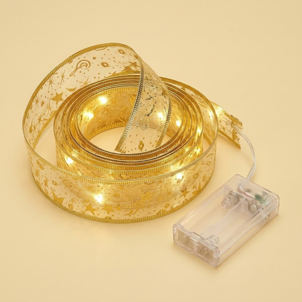 Coiled sheer gold ribbon light string with star patterns glows warm white beside a clear battery box on a cream background.