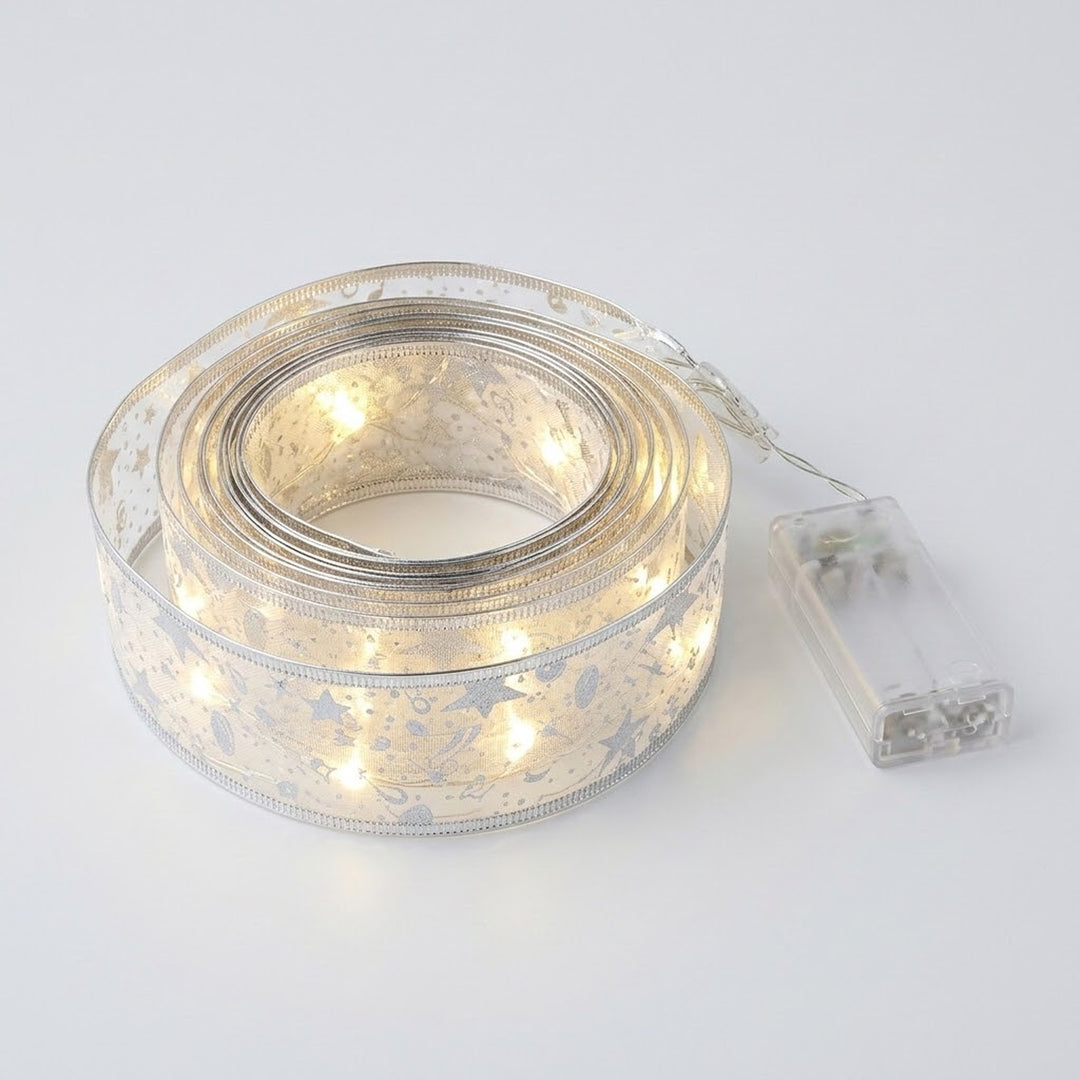 Coiled silver patterned ribbon light string glows warm white beside a connected clear battery box on a pale gray background.