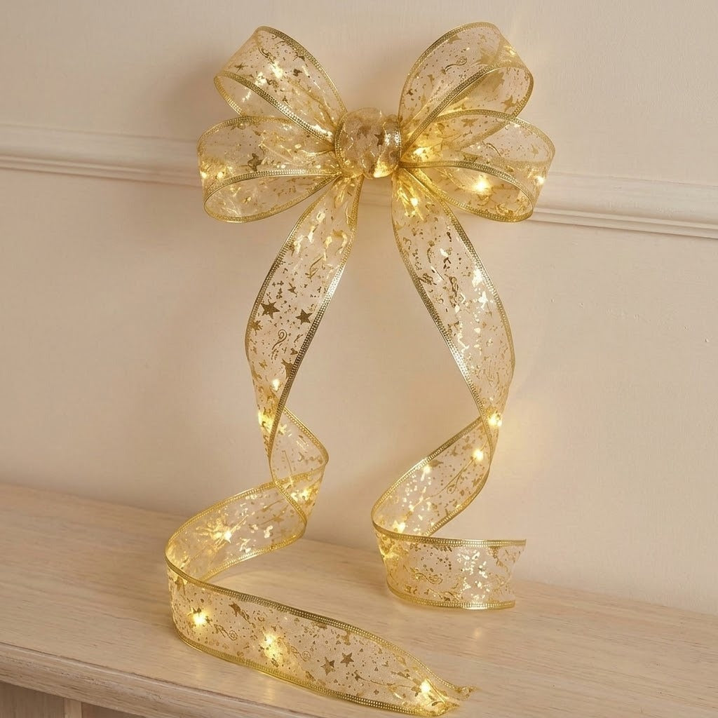 Sheer gold ribbon light string forms a glowing bow against a cream wall, with patterned tails curling onto a wooden surface.
