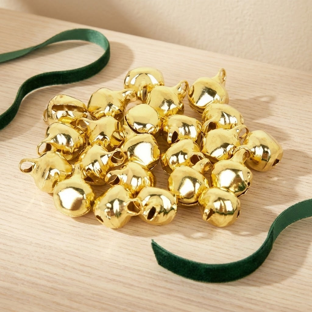 Shiny gold-color jingle bells with hanging loops form a pile between dark green ribbons on a pale wooden surface.