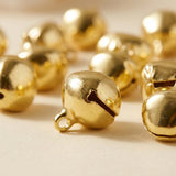A gold-color jingle bell rests on pale wood, showing its hanging loop and curved slit against blurred matching bells.