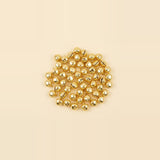 Gold jingle bells with narrow slits and small hanging loops lie clustered in the center of a cream background.