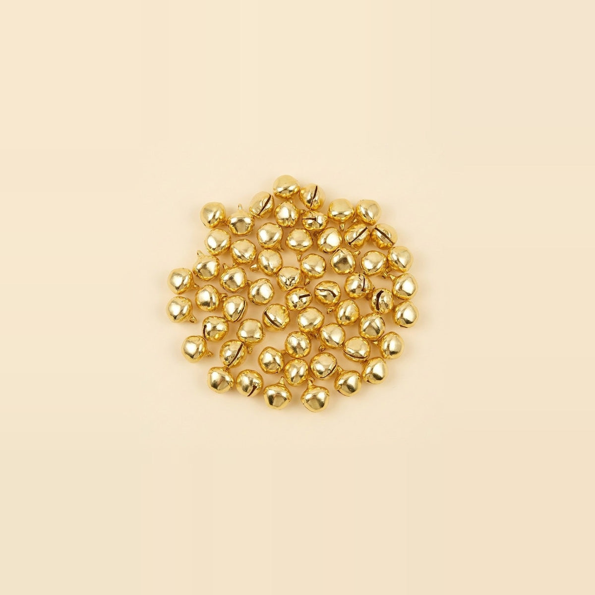 Gold jingle bells with narrow slits and small hanging loops lie clustered in the center of a cream background.