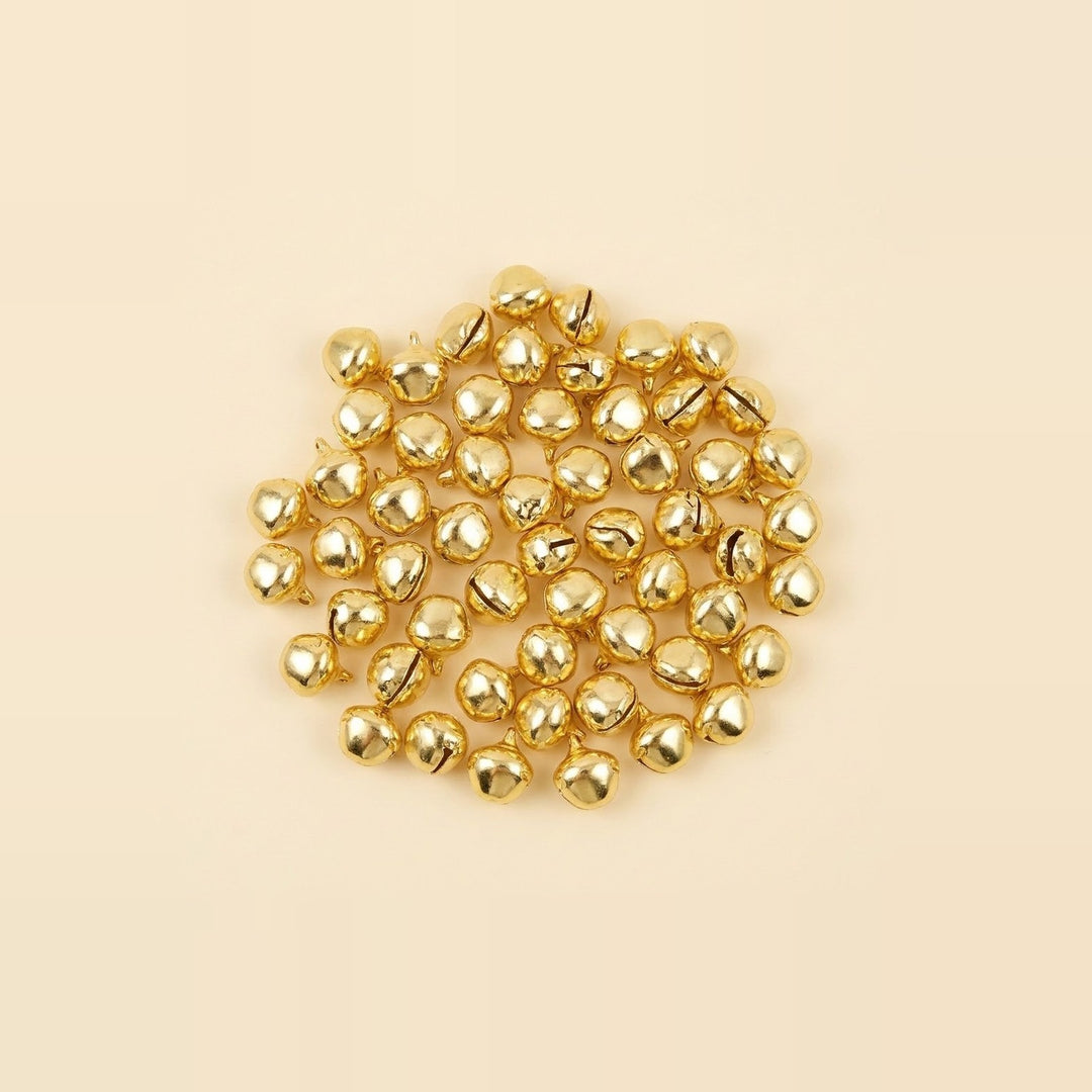 Reflective gold jingle bells lie in a loose rounded arrangement on a plain pale cream surface.