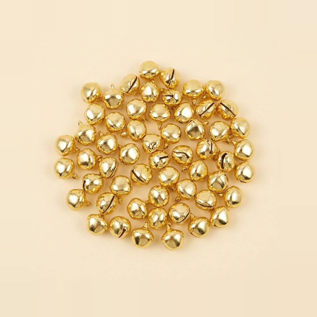 A broad cluster of shiny gold jingle bells shows rounded shells, dark slits, and hanging loops against a cream background.