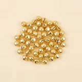 A broad cluster of shiny gold jingle bells shows rounded shells, dark slits, and hanging loops against a cream background.