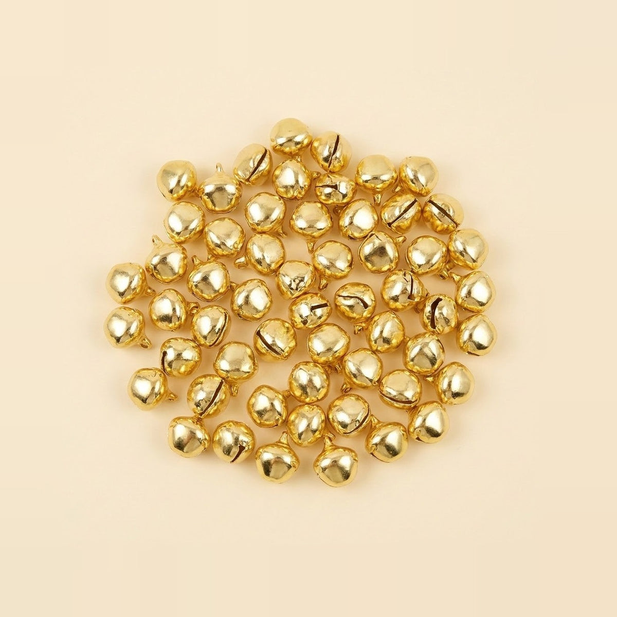 A broad cluster of shiny gold jingle bells shows rounded shells, dark slits, and hanging loops against a cream background.