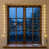 Warm white curtain lights hang over a wooden window, with a remote on the sill and clear USB controller at the side.