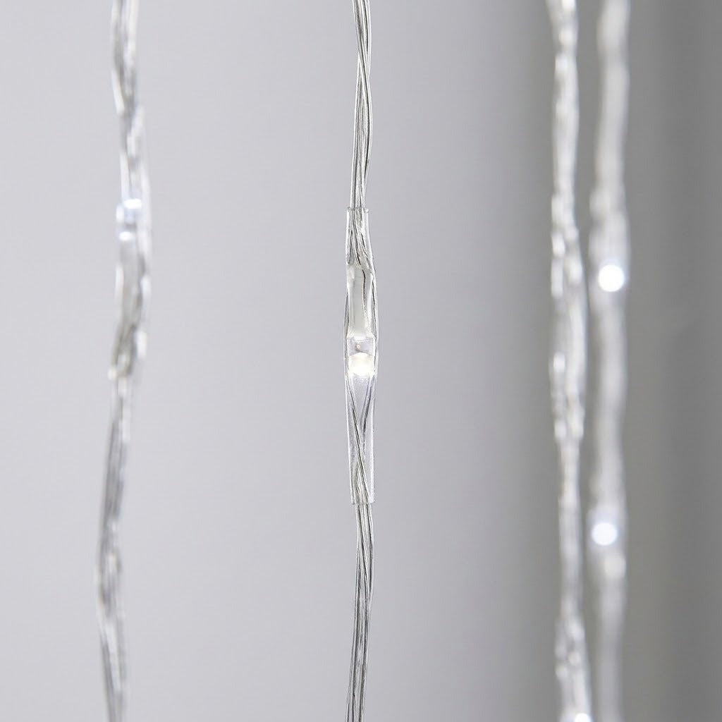 Curtain lights feature glowing white LEDs in clear coverings along thin silver-colored wires, shown close up against a blurred gray background.
