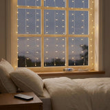 Warm white curtain lights cover a bedroom window, with a clear USB controller on the sill and remote on a wooden bedside table.
