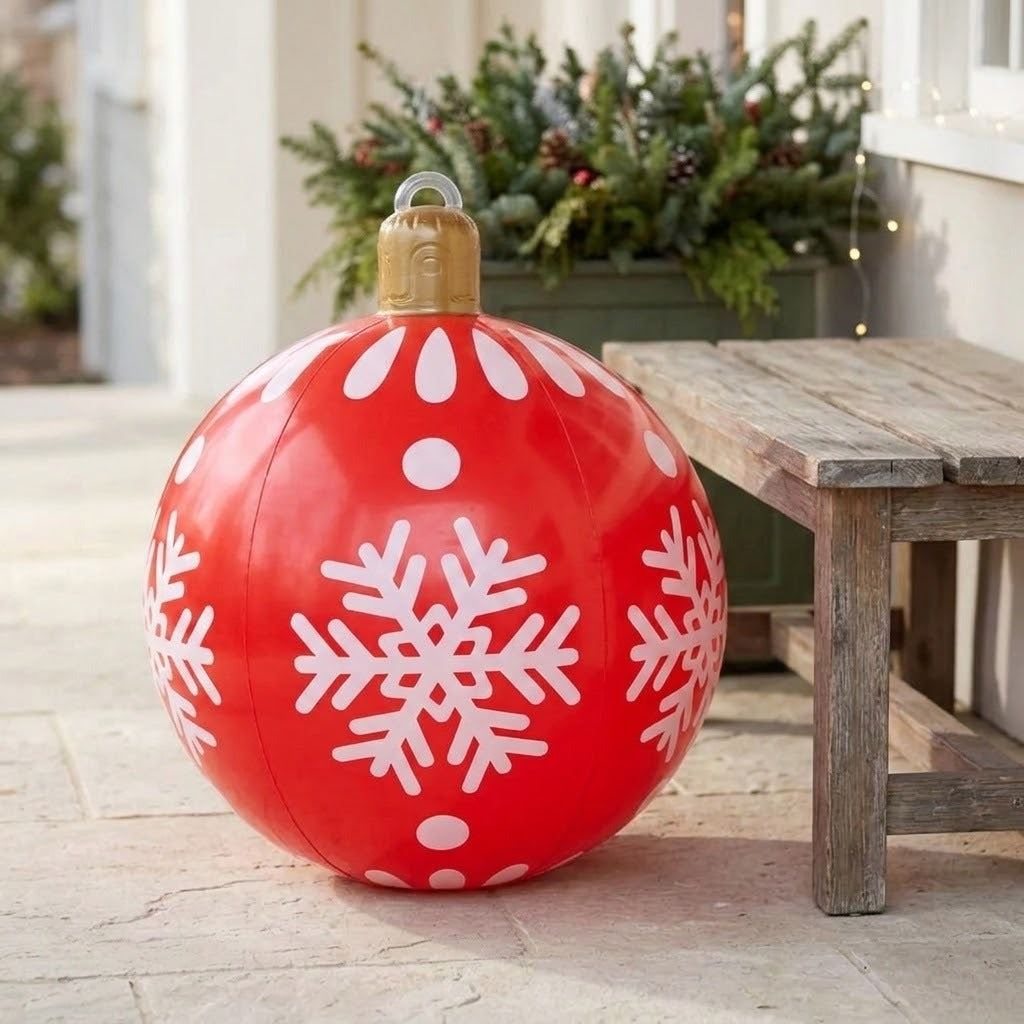 A red inflatable Christmas ornament with white snowflakes and a gold cap stands beside a wooden bench on a porch.