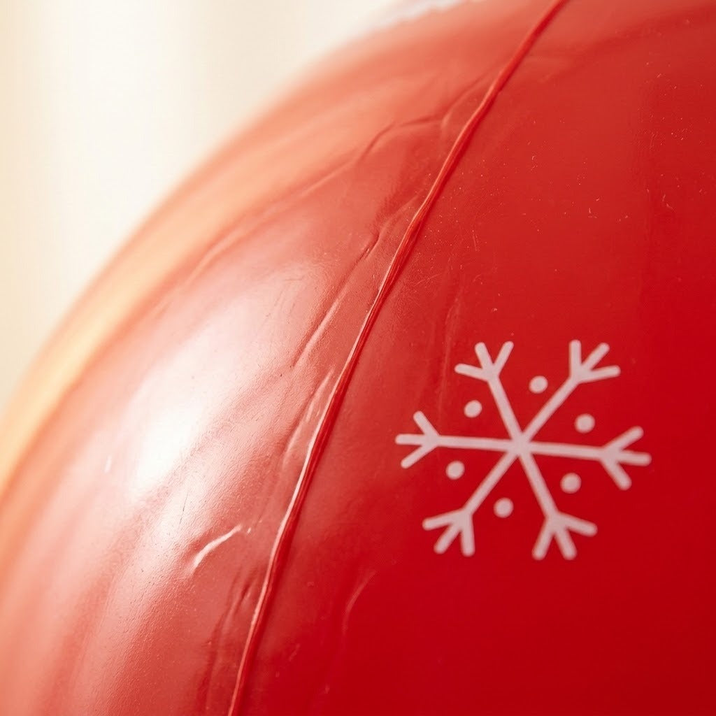The red PVC surface of an inflatable Christmas ornament shows a raised seam, small wrinkles, and a white snowflake in close-up.