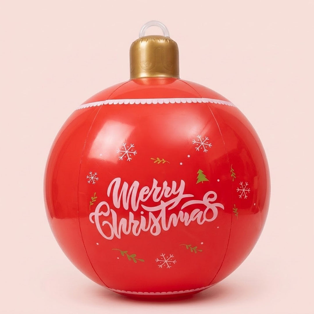 A red inflatable Christmas ornament displays white Merry Christmas lettering, snowflakes, gold trees, and a gold cap against a pale pink background.