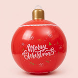 A red inflatable Christmas ornament displays white Merry Christmas lettering, snowflakes, gold trees, and a gold cap against a pale pink background.