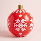 A red inflatable Christmas ornament with white snowflakes, dots, and a gold cap stands against a pale pink background.