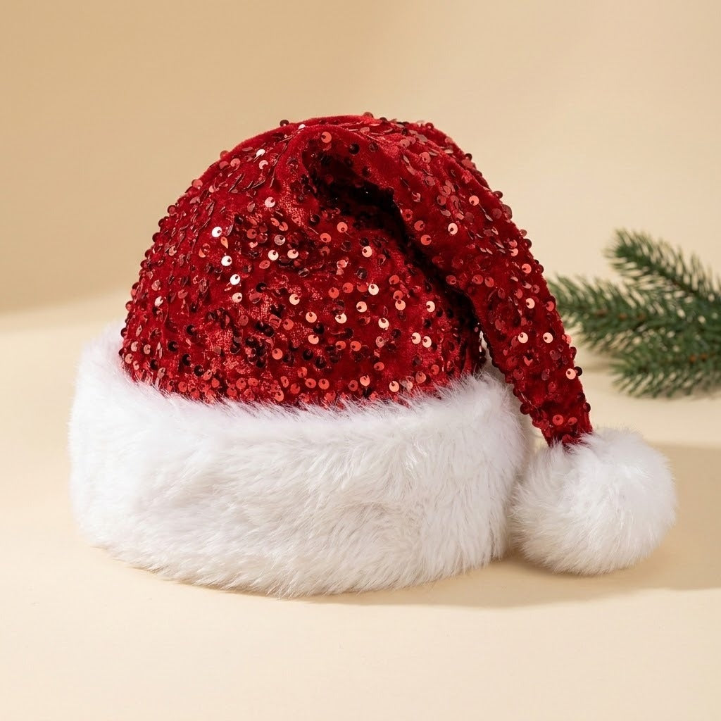 A festive Santa hat with a red sequined crown and a fluffy white faux-fur brim and pom-pom, photographed on a warm beige background with a small green pine branch prop at the side.