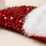 Close-up of a red sequin Santa hat with a fluffy white brim resting on a light beige surface.