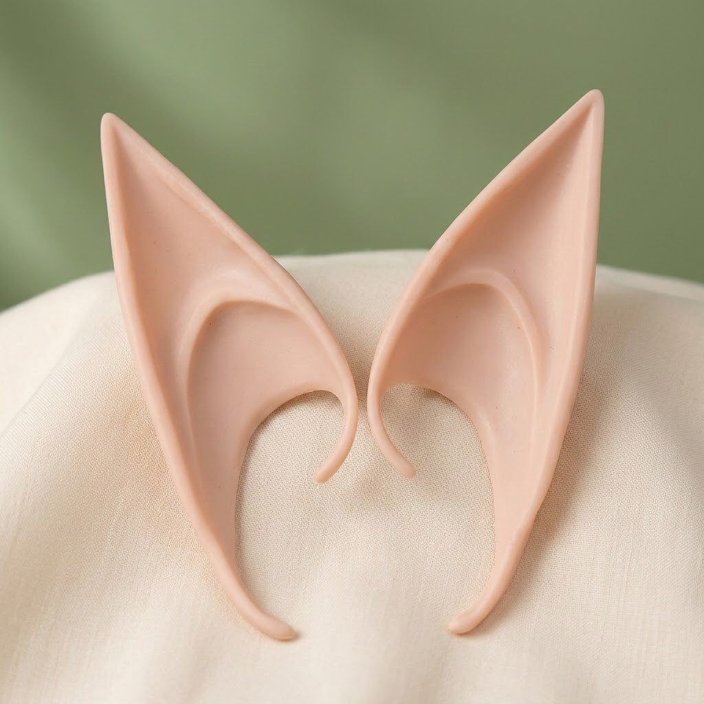 Peach latex elf ears with pointed tips and curved openings sit on cream fabric against a blurred green background.