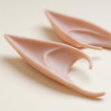 Peach latex elf ears shown close up on a cream surface reveal sculpted inner curves and thin edges.