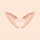 Light peach latex elf costume ears with curved hooks lying side by side on a pale peach background, 4.72 in (12 cm) pair.