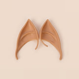 Warm tan latex elf costume ears with curved hooks lying side by side on a cream background, 3.94 in (10 cm) pair.