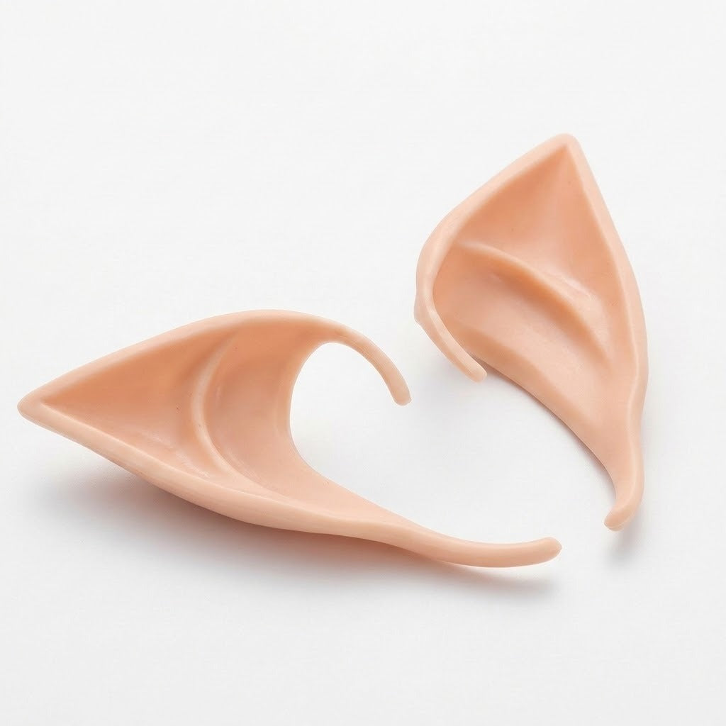 Two peach latex elf ears rest on a white surface, one sideways to reveal its thin edge and curved opening.