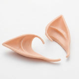Two peach latex elf ears rest on a white surface, one sideways to reveal its thin edge and curved opening.
