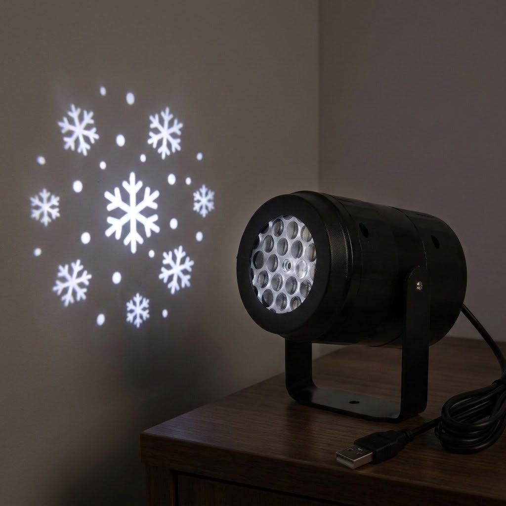 A black projector on a dark wooden table casts white snowflakes onto a wall, with its coiled USB cable alongside.