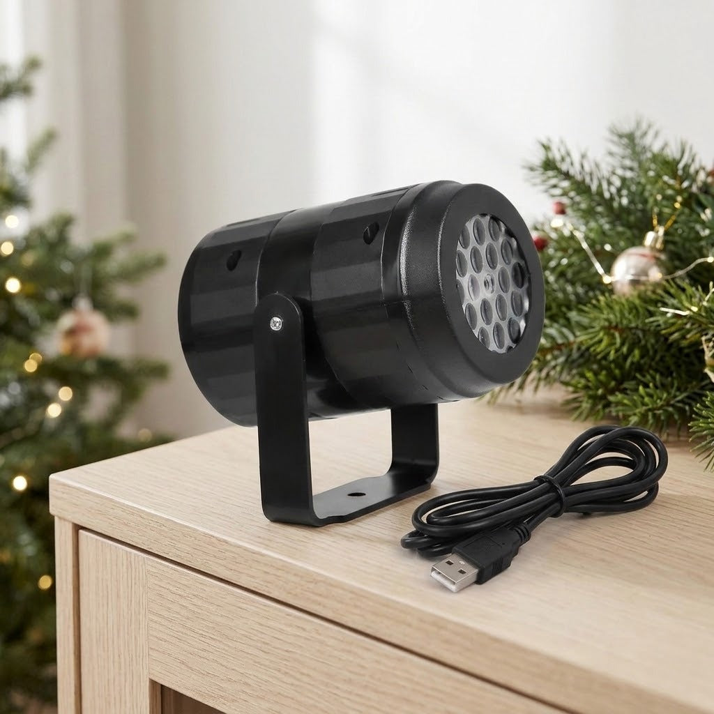 A black snowflake projector and coiled USB cable sit on a pale wooden cabinet beside Christmas greenery, ornaments, and string lights.