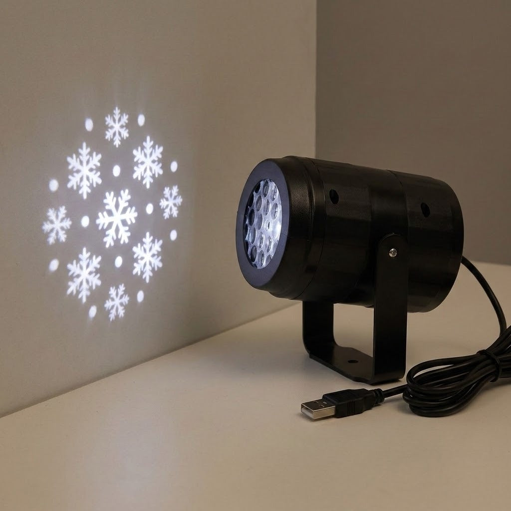 A black projector on a white tabletop casts white snowflakes onto a beige wall, with its USB plug and coiled cable visible.