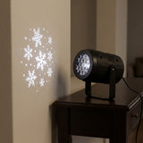 A black projector stands on a dark wooden console table, casting white snowflakes and dots onto a nearby cream wall.