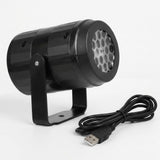 A black snowflake projector faces right on its U-shaped stand with a coiled USB cable in front against a white background.