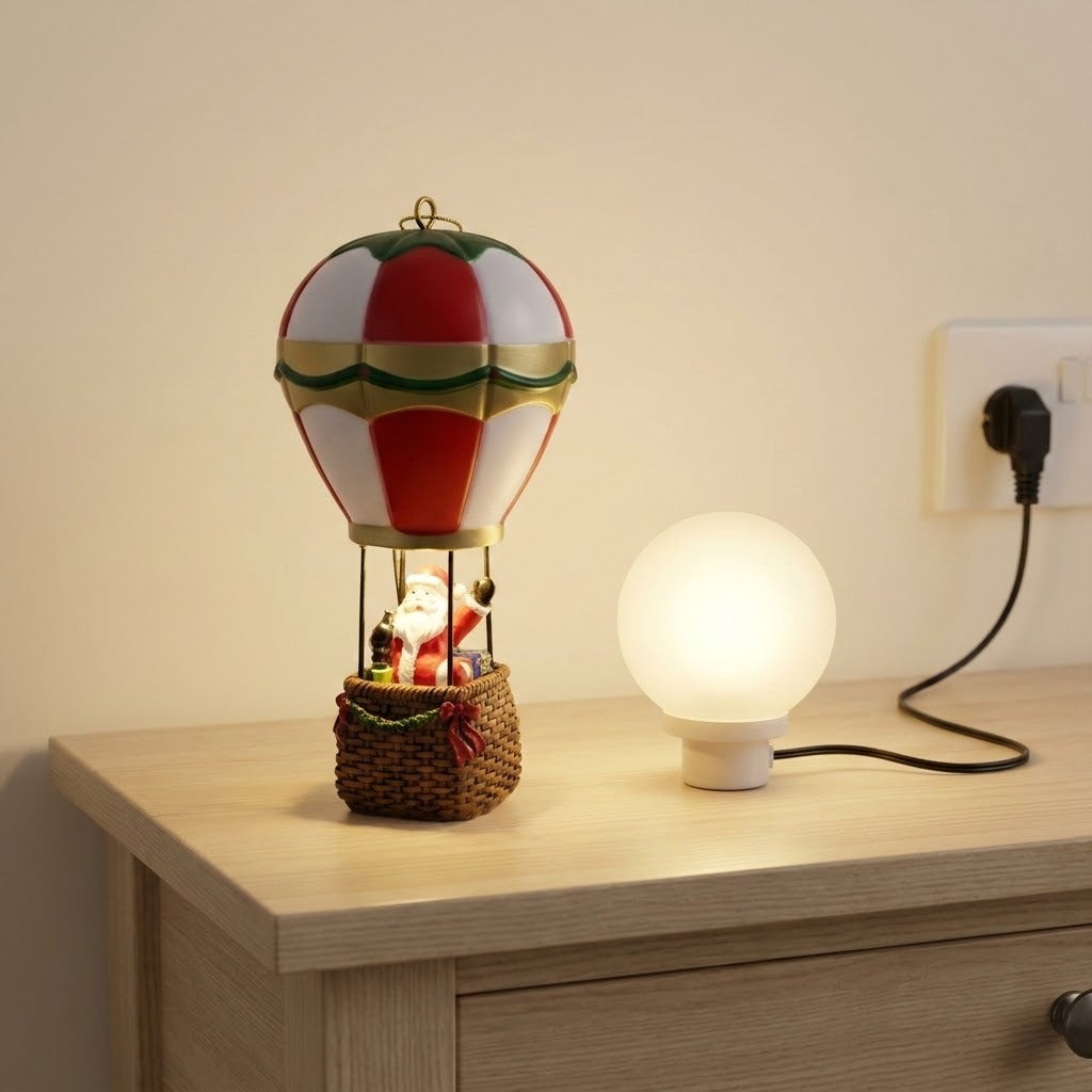 Red and white Santa hot air balloon Christmas decorative light stands beside a glowing round lamp on a wooden cabinet.