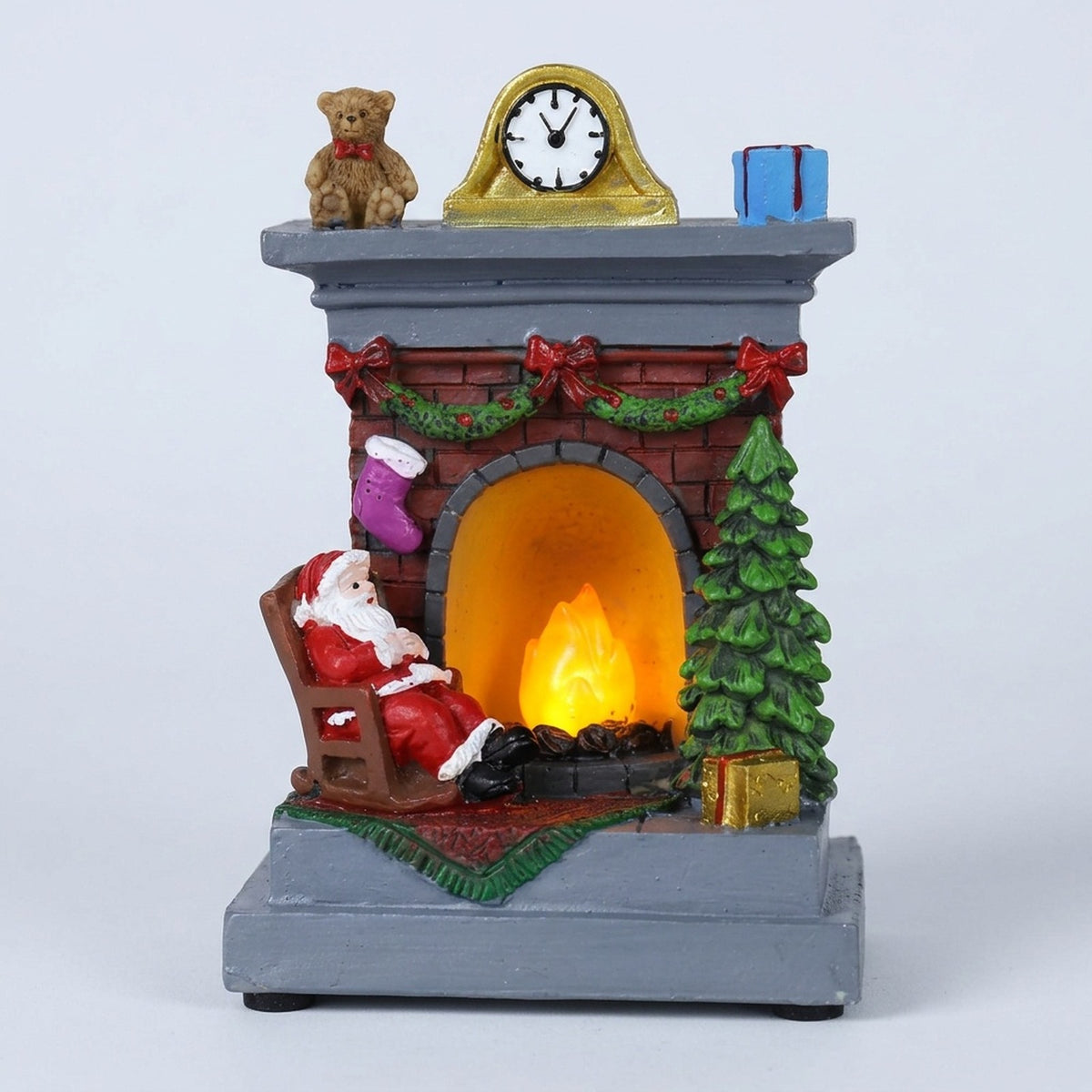Christmas decorative light featuring red-suited Santa beside a glowing brick-style fireplace, green tree, and gray mantel against a white background.