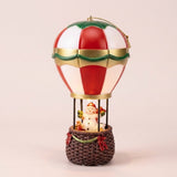 Snowman hot air balloon Christmas decorative light has red and white panels, gold and green trim, and a brown basket against pale pink.