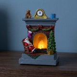 A Santa fireplace Christmas decorative light with a gray base and glowing orange hearth stands on dark wood against a blue wall.