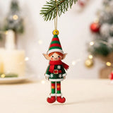 A flat wooden elf Christmas ornament in red and green hangs by gold string from an evergreen branch against a blurred festive background.