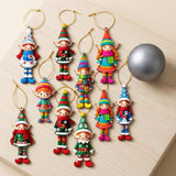 Nine colorful flat wooden elf Christmas ornaments with gold hanging strings lie on a pale wooden board beside a matte gray bauble.
