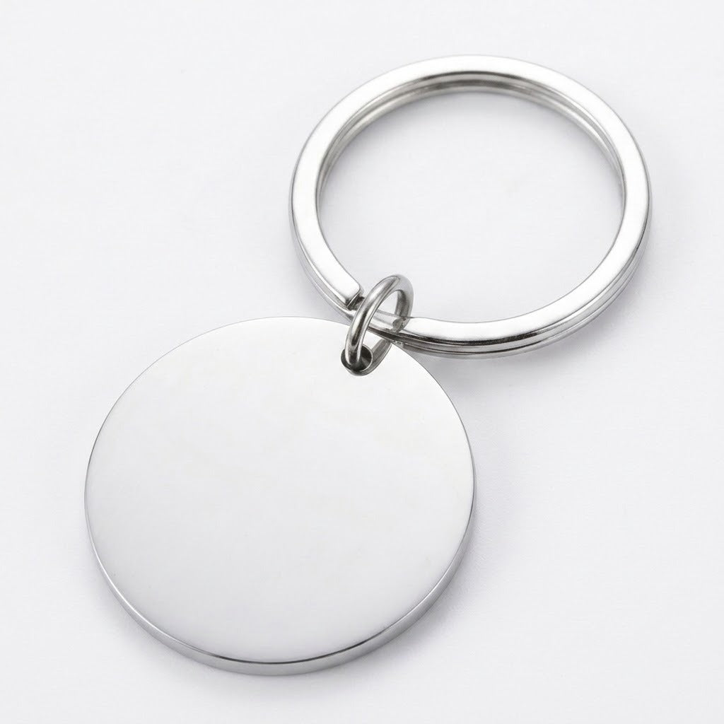 Silver keychain with a plain circular pendant reverse, small connector ring, and round split ring lies diagonally on a white background.